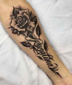 a black and white rose tattoo on the left arm with writing below it that reads,