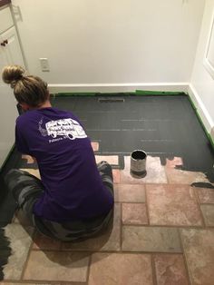 a woman sitting on the floor painting a room with gray tile and green trimmings