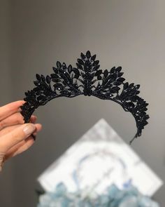 a woman holding up a black tiara in front of a white and gray background