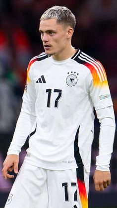 a soccer player in white and black uniform standing on the field with his hands behind his back