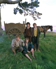 three young men are posing in front of a horse drawn wagon