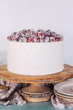 a white cake topped with cranberries on top of a wooden platter next to plates