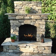 a stone fireplace with potted plants on it in the middle of a garden area