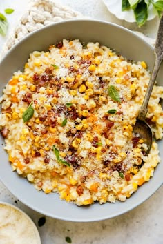 a white bowl filled with corn and topped with parmesan cheese next to a spoon