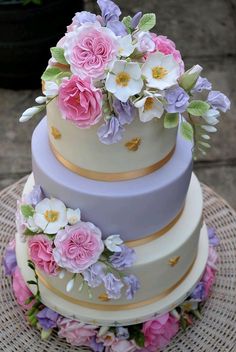 a three tiered cake with flowers on the top and bottom, sitting on a wicker table