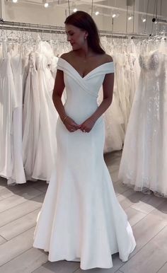 a woman in a white wedding dress standing next to some dresses on display at a bridal