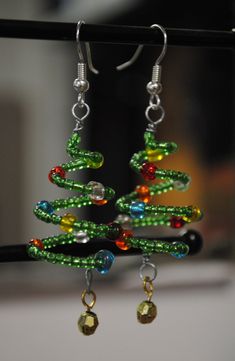 a pair of christmas tree earrings hanging from a hook on a black wire with green, red and yellow beads