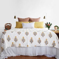 a white bed with yellow and brown pillows in a bedroom next to a wooden table