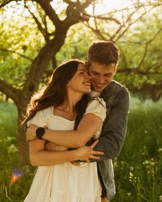 a young man and woman embracing each other in front of a tree with sunlight shining through the leaves