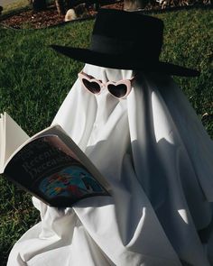 a ghost reading a book in the grass with sunglasses on it's face and wearing a black hat