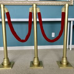 two gold poles with red rope on them in front of a blue wall and window