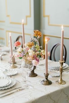 an elegant table setting with candles and flowers in vases on the centerpiece, along with plates and silverware