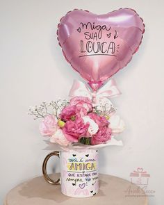 a pink heart shaped balloon sitting on top of a coffee mug filled with flowers and balloons