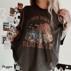 Stand out at the rodeo or country music festival with this "Ain't Going Down" shirt. Perfect for the cowgirl in your life, this Western retro tee features a unique graphic inspired by Garth Brooks' hit "Til the Sun Comes Up." Made with comfort colors, this cowboy shirt is a great gift for her and an essential addition to any country music lover's wardrobe. Get your hands on this stylish and trendy piece that combines classic Western vibes with a touch of modern flair. A must-have for those who love to embrace their country roots in style. Our team at The Southern Thistle is always happy to bring your ideas to life. If you have a custom design in mind, please send us a message or email us at info@thesouthernthistle.com to discuss your vision. With a 5-star rating, you can trust in the quali Country Music Shirt, Country Music Festival, Western Vibes, Country Music Shirts, Rodeo Shirts, Cowboy Shirt, Garth Brooks, Cowboys Shirt, Country Shirts