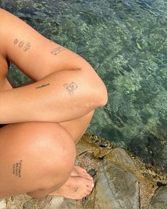 a woman sitting on rocks next to the water with her legs crossed and tattoos tattooed