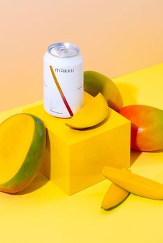 a can of drink next to sliced mangoes and kiwis on a yellow surface