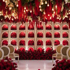 a room filled with lots of red flowers and white chairs in front of a wall