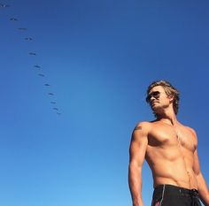 a man with no shirt standing in front of a flock of birds on a clear blue sky