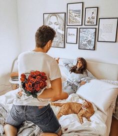 a man sitting on a bed with flowers in his hand and a cat laying next to him