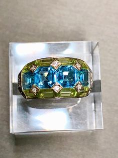 A beautifully made ring done in 18K yellow gold that has been set with 3.35cttw in blue topaz, 2.46cttw, 2.46cttw in green peridot and .09cttw in H-I color Si1-2 clarity diamonds... such a color combination! All weights are stamped inside of the shank. Dimensions/Weight: Ring measures .45" top to bottom and weighs 10.8g. Size 6 (sizable). Condition: All stones are secure and in perfectly wearable condition. R-TYE Luxury Green Topaz Gemstone Ring, Green Multi-stone Topaz Ring For Formal Occasions, Formal Green Topaz Ring With Accent Stones, Green Blue Topaz Gemstone Rings, Formal Green Multi-stone Topaz Ring, Green Peridot, Color Combination, Rings Statement, Blue Topaz