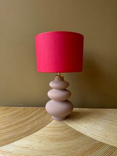 a pink lamp sitting on top of a wooden table next to a red lampshade