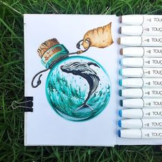 an open notebook with markers and pens on the pages that have drawings in them, including a drawing of a whale inside a glass jar