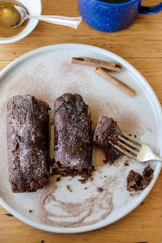 two pieces of chocolate cake on a white plate next to a cup of coffee and spoon