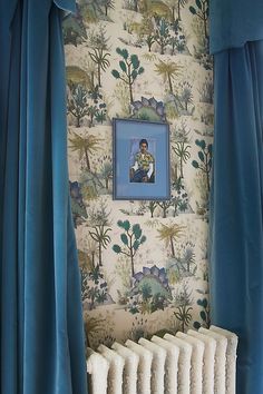 a painting hangs on the wall next to a radiator in a room with blue curtains