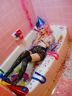 a woman laying in a bathtub with lots of confetti on the floor