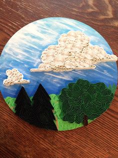 a paper plate with trees and clouds in the sky on top of a wooden table