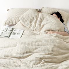 a woman laying in bed with an open book on her side and the covers pulled back