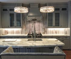 a large kitchen with marble counter tops and two lights hanging over the island in front of it