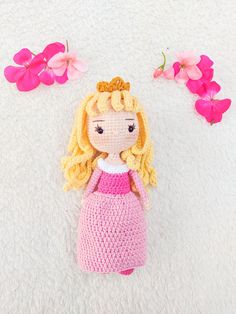 a crocheted doll laying on top of a white blanket next to pink flowers