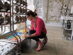 a woman kneeling down next to a rack filled with pots and pans on display