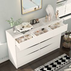 a white dresser with drawers and various items on it in a room next to a rug