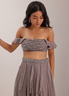 This stunning Grey Off-Shoulder Embellished Skirt Set, made from luxurious shimmer chiffon, flows gracefully with every step. The high-waisted grey skirt with an embroidered waistband features a daring thigh-high slit, adding a bold, modern twist to its elegant design. Teamed with an off-shoulder blouse is adorned with intricate crystal work and delicate frills, giving it a soft, feminine look while adding a touch of sparkle. Ideal for Sangeet, cocktail events, or evening parties, this outfit exudes sophistication and glamour. Composition : Skirt, Blouse - Chiffon and Shantoon Care: Dry Clean Only and Vacuum Storage This product can be customized for sleeves, blouse length and neckline Delivery : 4-6 weeks as the product is hand crafted. Check Size Guide or choose MySize for free customisa Crystal Work, Blouse Chiffon, Embellished Skirt, Grey Skirt, Skirt Blouse, Vacuum Storage, Soft Feminine, Sleeves Blouse, Feminine Look