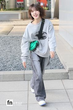 a woman walking down the street with a green bag on her shoulder and wearing grey sweatpants