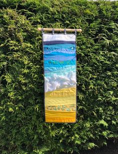 a banner hanging on a bush with the ocean and beach scene painted on it's side