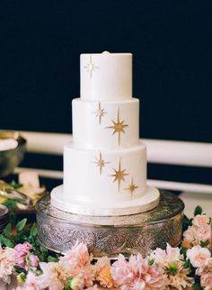 a three tiered white cake with gold stars on the top and pink flowers around it