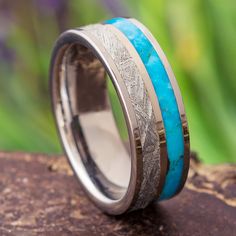 a wedding band with blue and silver inlays on top of a tree stump