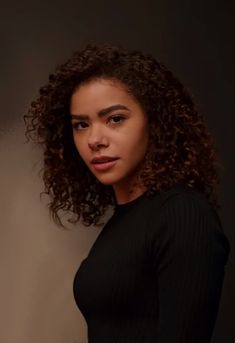 a young woman with curly hair posing for a photo in front of a dark background