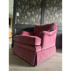 a pink chair sitting in front of a wall with floral designs on it's walls