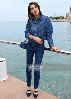 a woman standing on the edge of a pier wearing blue denim clothes and black heels