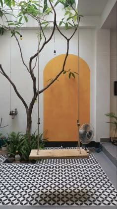 an indoor area with a tree, swing and potted plants on the floor in front of a yellow door