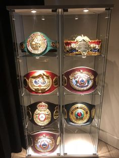 a display case filled with lots of different types of boxing belts on glass shelves in front of a black curtain