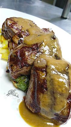 some meat and vegetables on a plate with gravy over them, ready to be eaten