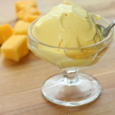 a glass bowl filled with ice cream next to sliced pineapple on a wooden table