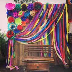 a wooden bench covered in colorful streamers next to a wall with flowers on it