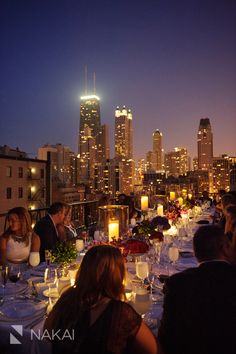 a group of people sitting at a table with candles in front of the city skyline