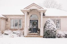 a house with snow on the ground and bushes around it, in front of a door